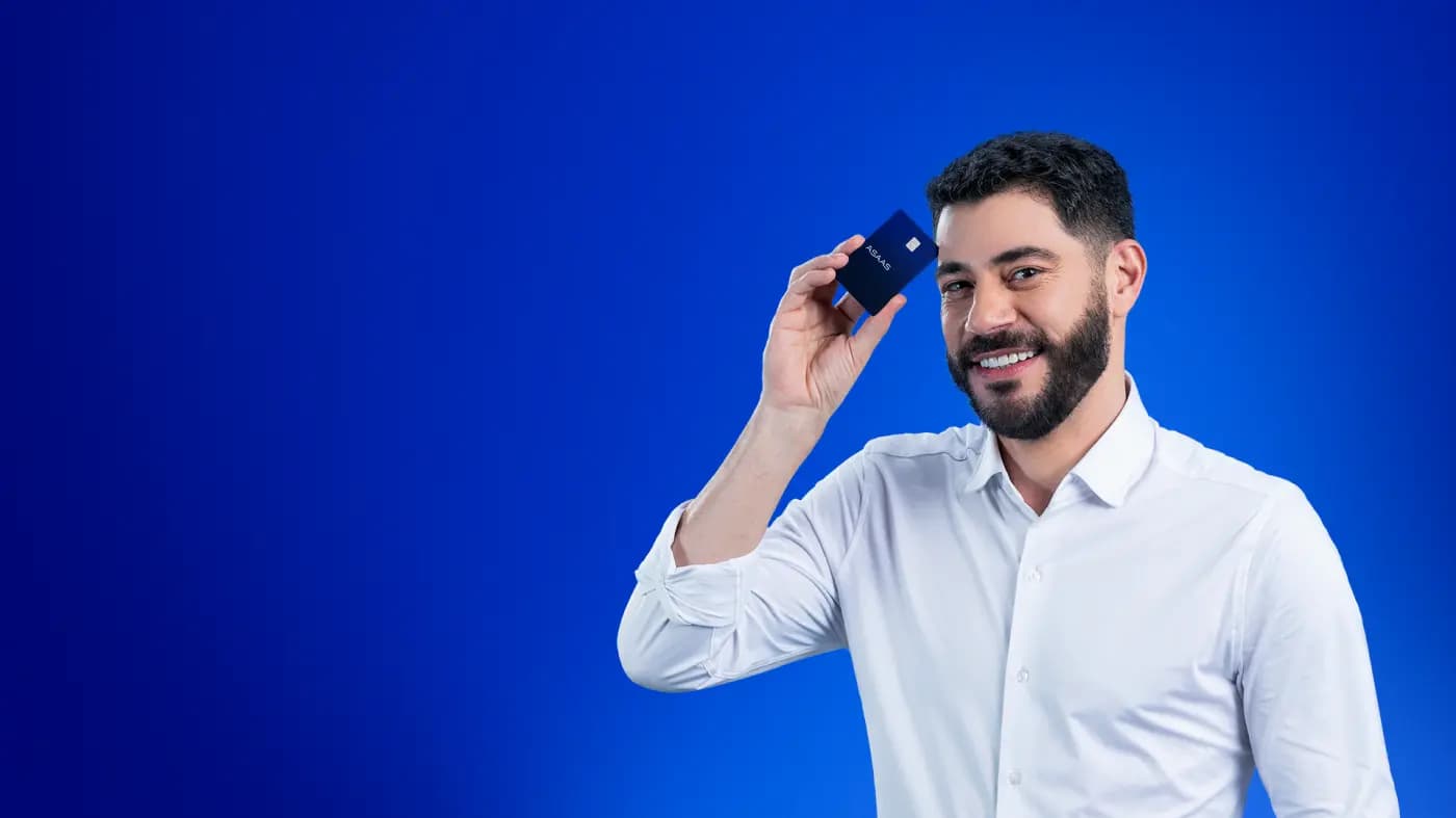 Evaristo Costa veste uma camisa social branca e está sorrindo para a câmera segurando um cartão Asaas ao lado do rosto.