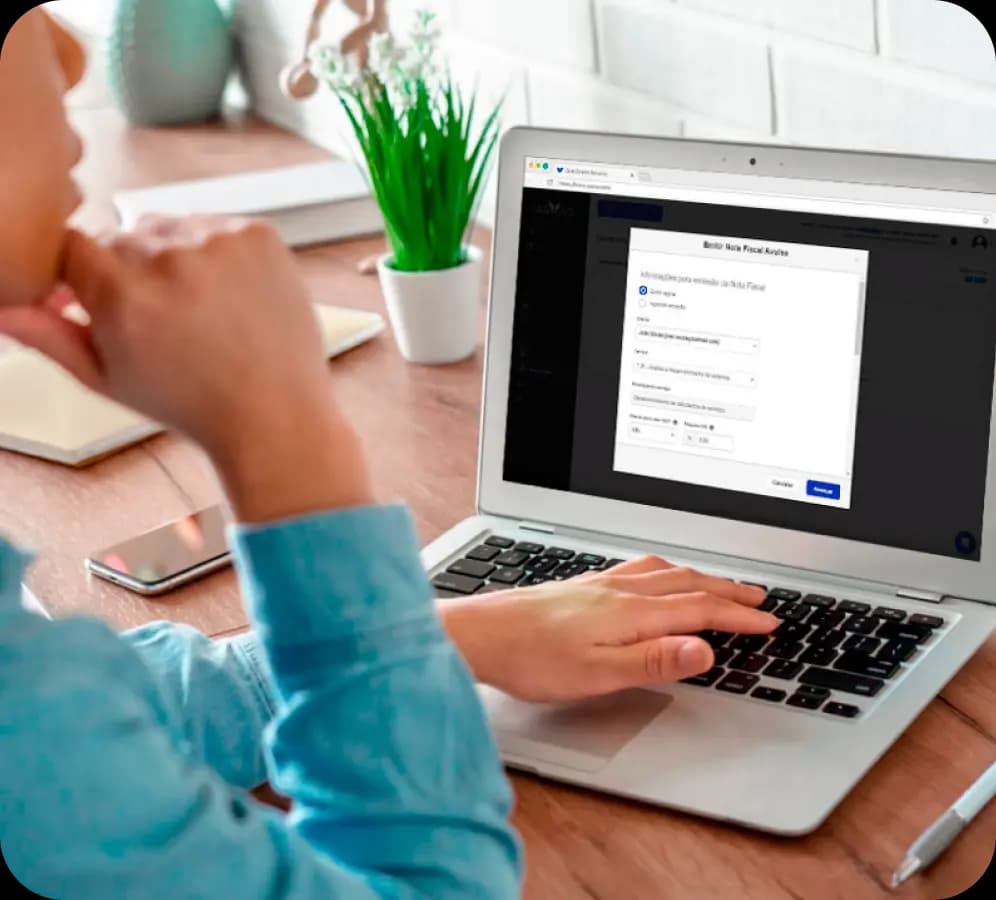 Mulher está sentada mexendo no notebook, que exibe a tela de emissão de nota fiscal do Asaas.