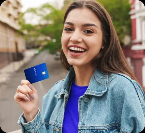 Empreendedora sorri para a câmera enquanto segura o Cartão Asaas. Ela tem cabelos longos, lisos e castanhos, pele clara, e veste uma camiseta azul e jaqueta jeans.