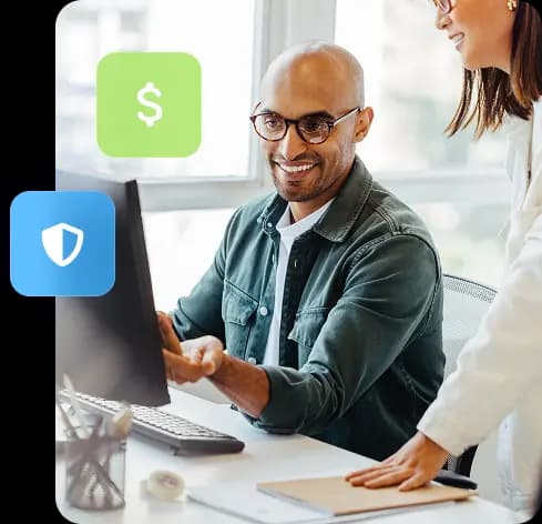 Homem sentado em uma mesa de escritório apontando para um monitor de computador a sua frente. Uma colega de trabalho está olhando para o que ele está apontando.