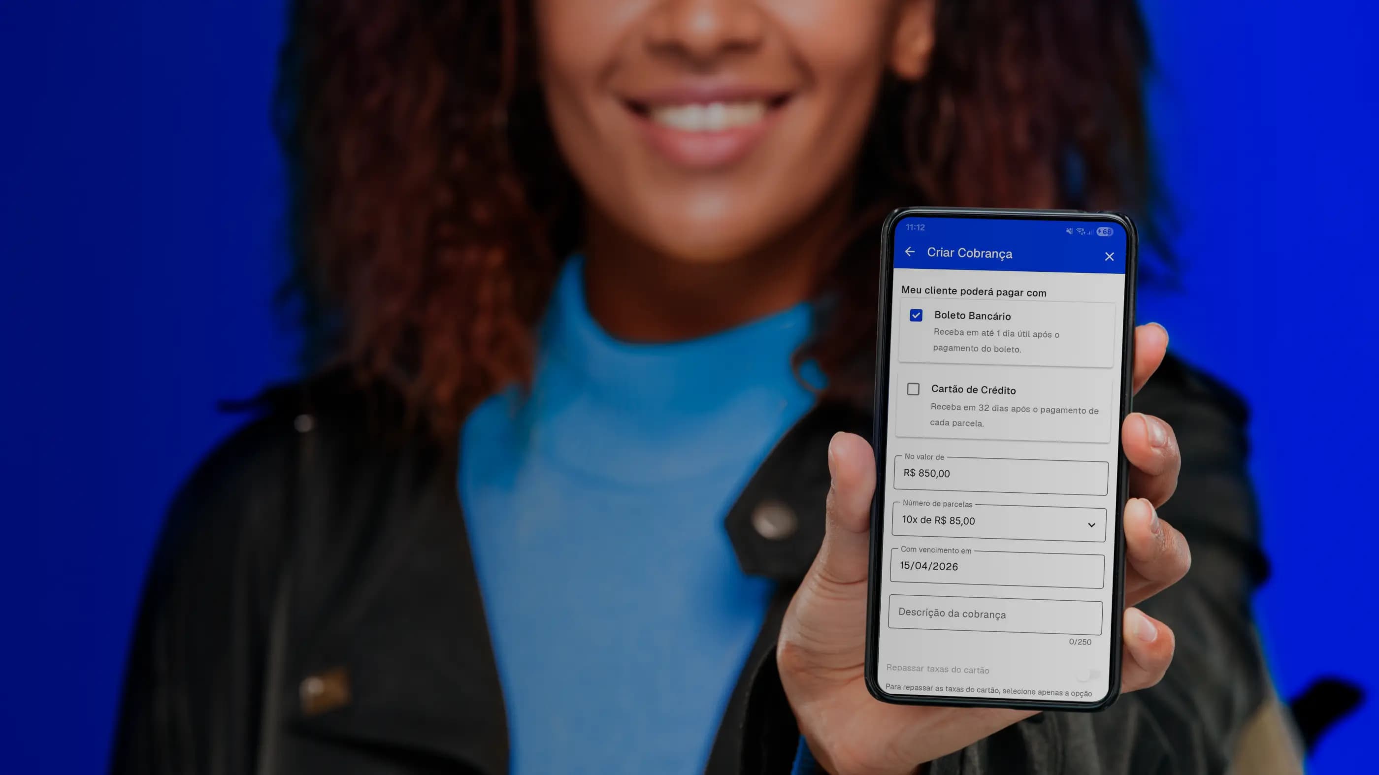 Mulher sorri, mostrando o celular que está segurando na mão, na tela está a página de emissão de boleto bancário do Asaas.