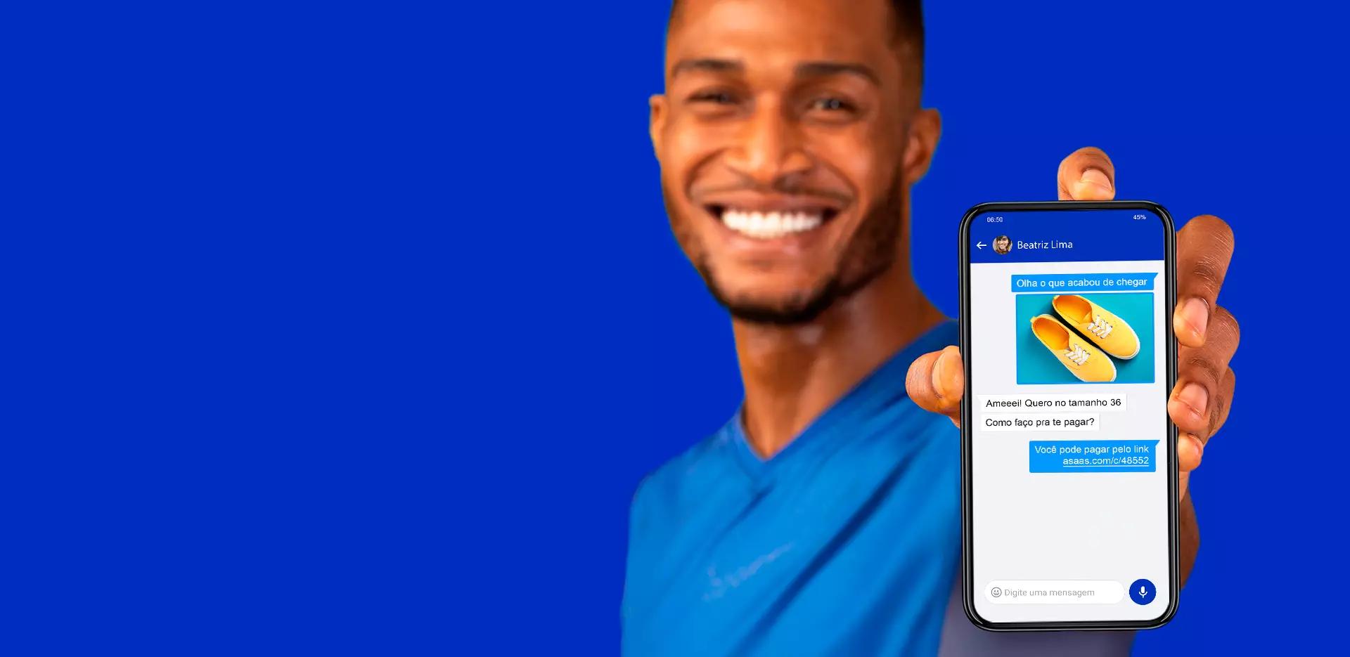 Homem sorri para a câmera enquanto segura um celular que mostra a tela de criação de link de pagamento.